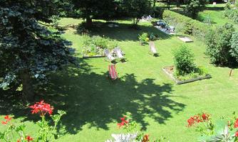 A beautiful garden with a green lawn and colorful lounge chairs. Surrounded by trees and flower beds, it invites you to relax.