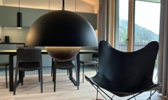 A stylish dining room with a modern lamp and elegant chairs. In the background, large windows offer a view of the mountains.