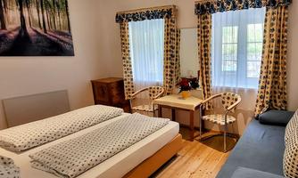 A bright room with two beds, a table, and chairs. Large windows let in plenty of light and create a cozy atmosphere.