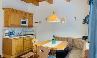 A cozy kitchen with wooden cabinets and a dining area. A table with seating and a blooming plant serves as the centerpiece of the room.
