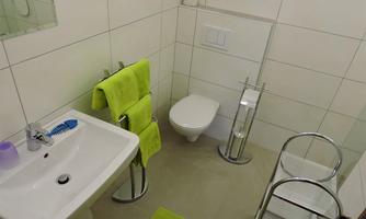 A modern bathroom with bright tiles. It includes a sink, a toilet, and green towels.