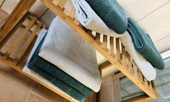 A wooden shelf with neatly stacked towels in various colors. The towels are in soft shades of green and gray.