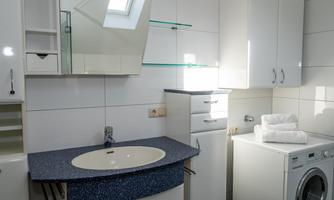 A modern bathroom with a sink and a mirror. A washing machine and towels are also visible.