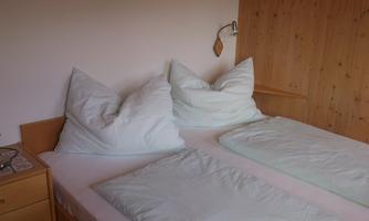 A simple bedroom with two beds and large pillows. The walls are made of wood and there is a nightstand with a lamp.