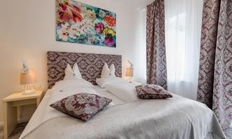 A stylish bedroom with a large bed and decorative pillows. The walls are adorned with appealing curtains and a colorful mural.