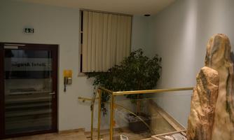 A bright entrance area with a staircase and a plant in the corner. In the background, the entrance door is visible with the inscription "Hotel."