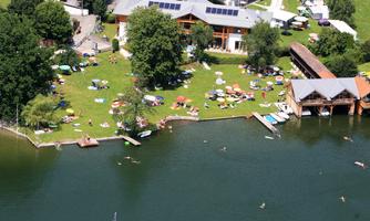 A picturesque lakescape with boats and a beautiful green space. There are loungers and a holiday atmosphere in the surroundings.
