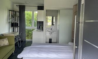 A modern room with a double bed and a large window front. The decor is simple and functional with a cozy sofa.