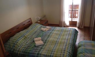 A cozy bedroom with a large bed and a small single bed. The walls are bright and the window lets in plenty of daylight.