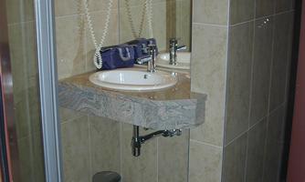 A small bathroom with a shower and a modern sink. The walls are tiled with beige tiles.