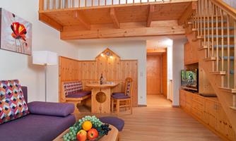 A cozy apartment with wooden interiors and an open staircase. The living area is bright and inviting, featuring a dining area and a fruit bowl.