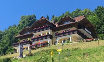A charming house with multiple balconies, surrounded by green nature. The facade is decorated with flowers and it radiates a friendly atmosphere.
