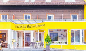 A yellow inn with the sign "Gasthof zur Post". There are outdoor tables and windows with wooden frames.