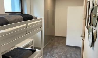 A modern bedroom with a loft bed and a bright, minimalist decor. The room has a neutral tone and plenty of daylight.