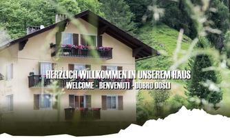 An inviting house amidst green mountains. The inscription welcomes guests in various languages.