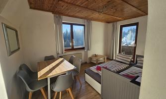 A cozy room with a dining area and a couch. Large windows provide a view of the surrounding nature.