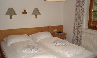 A cozy bedroom with two single beds and a bright, friendly ambiance. The walls are painted in soft colors and decorated with floral curtains.