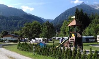 A beautiful campsite in the mountains with caravans and a playground. The landscape is green with mountains in the background and a clear sky.