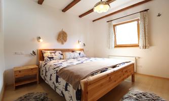A cozy bedroom with a large wooden bed and a windowsill. The walls are light and there is soft lighting as well as decorative elements.
