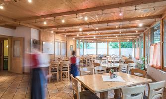 A cozy restaurant with wooden decor and large windows. Tables are nicely set, and there is a hint of movement in the room.