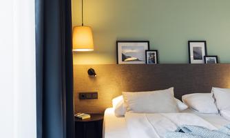 A cozy bedroom with a large bed and soft lighting. Framed pictures hang on the wall, and there is a nightstand.