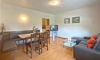 A cozy living room with a modern couch and a dining area. The walls are simple and painted in warm colors.