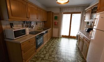 A cozy kitchen with wooden cabinets and a window that lets in a lot of light. On the countertop, a microwave and a stove are visible.