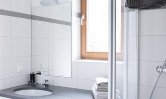 A modern bathroom with white tiles and a window. A few fresh towels are placed on the sink.