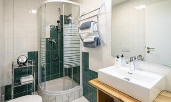 A modern bathroom with a shower cabin and a sink made of white ceramic. The walls are light tiled, and there are wooden details for a warm accent.