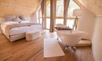 A cozy bedroom with a large bed and a modern bathtub. Large windows offer a beautiful view of nature.