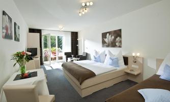 A modern hotel room with two beds, elegant decor, and a small table. Large windows let in plenty of light and provide a view of the outdoors.