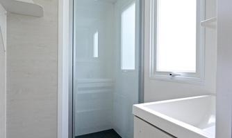 A modern bathroom with a glass shower and a sink. Bright walls and windows create a friendly atmosphere.