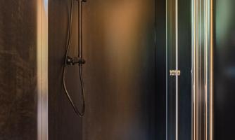 A modern shower with a black rain shower and glass partition. The walls are dark and the floor is white.
