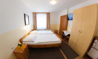 A bright and friendly hotel room with a double bed and wooden furniture. The windows let in plenty of daylight, and there is a small desk.