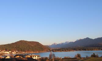 A picturesque landscape with a clear lake, surrounded by mountains and forests. The sky is blue and radiant.