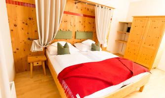 A cozy room with a double bed and a red blanket. The walls are made of wood and there are decorative curtains.