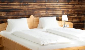A cozy bedroom with a double bed made of light wood. The walls are paneled with dark wood, and there is a small lamp next to the bed.