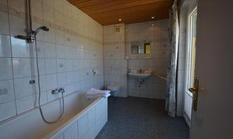 A modern bathroom with tiles and a wooden ceiling. It is equipped with a bathtub, shower, and sink.