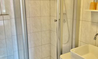 A modern bathroom with a glass shower cabin and a sink. The walls are decorated with white tiles.