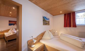 A cozy bedroom with two beds and wood paneling. The walls are light, with a window and artwork in the background.