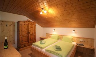 A cozy bedroom with wooden ceilings and wooden furniture. There are two beds with green bedding and a charming wardrobe wall.