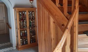A cozy entrance area with a curved wooden staircase. Next to the staircase is a display cabinet with many glasses.