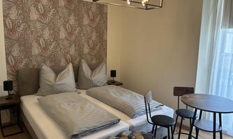 A modern bedroom with a double bed and elegant bedding. The room also features a table and chairs, as well as a beautiful light fixture. Overlooking the balcony door.