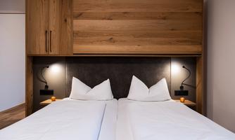 A modern bedroom with a double bed and white bedding. On the wall, there are elegant bedside lamps and wooden accents.