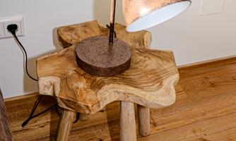 A beautiful wooden nightstand with a unique shape. On it sits a stylish lamp with a copper surface.