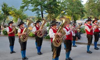 A group of musicians is playing on the street. They are wearing traditional costumes and playing large brass instruments.