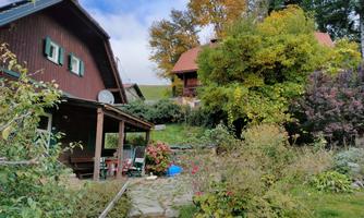 A picturesque house in the greenery with colorful autumn trees. The garden is lushly overgrown and invites you to linger.