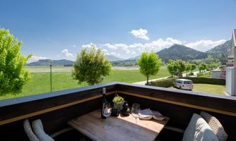 A beautiful view from a balcony overlooking a green landscape with trees and mountains in the background. The table is set for a relaxing break.
