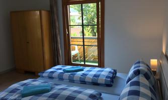 A cozy bedroom with two single beds and checked bedding. The window offers views of a small balcony and lush greenery.