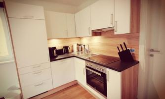 A modern kitchen with white cabinets and wooden accents. The equipment includes a stove, a sink, and electrical appliances.